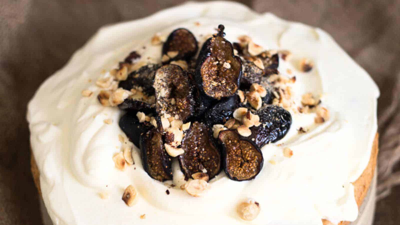 Cake topped with whipped cream, sliced figs, and chopped nuts on a brown background.