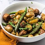 A bowl of Vegetarian Swamp Potatoes stew with green beans, hearty chunks, and fresh herbs, served beside an orange napkin.