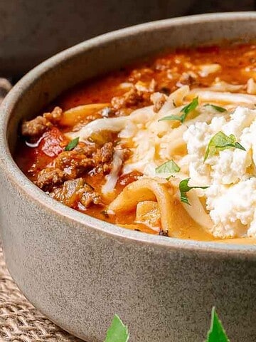 Bowl of lasagna soup topped with ricotta cheese and parsley, with a spoon inside the bowl.
