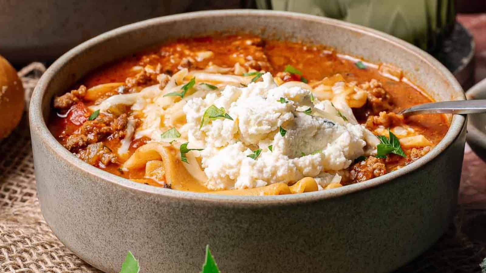 Bowl of lasagna soup topped with ricotta cheese and parsley, with a spoon inside the bowl.