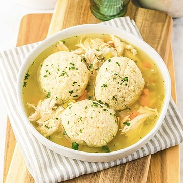 A bowl of chicken and dumplings soup with shredded chicken, vegetables, and three large dumplings on top, perfect for a cozy slow cooker recipe.