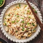 A plate of fried rice with peas, carrots, tender teriyaki chicken pieces, and green onions, served with chopsticks on the side—a delicious recipe perfect for any meal.