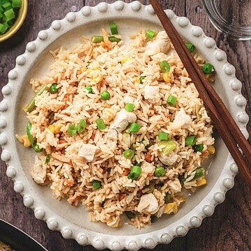 A plate of fried rice with peas, carrots, tender teriyaki chicken pieces, and green onions, served with chopsticks on the side&mdash;a delicious recipe perfect for any meal.