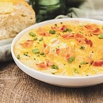 Creamy Crack Potato Soup topped with shredded cheese, bacon, and green onions in a white bowl on a wooden table.