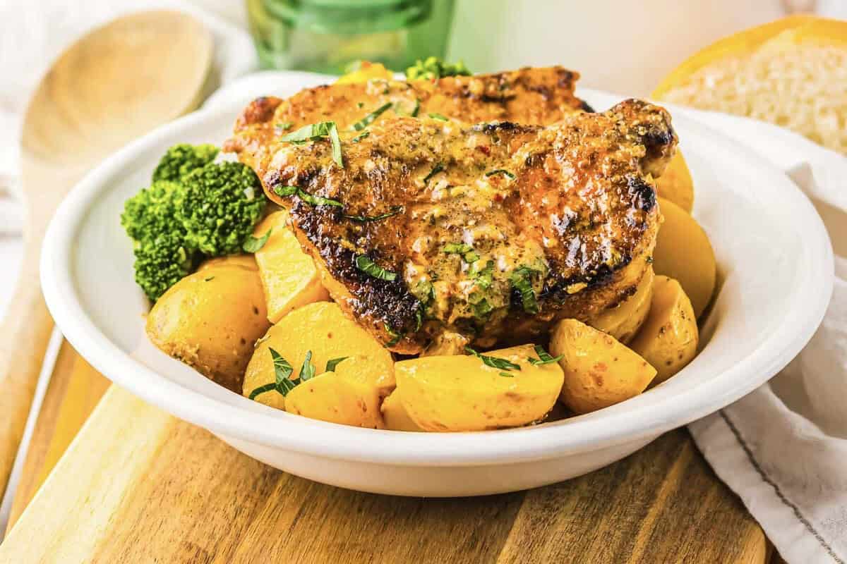 Garlic Parmesan pork chops with golden potatoes and broccoli served in a white bowl on a wooden board.