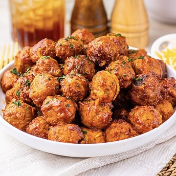 A bowl filled with saucy meatballs, garnished with herbs, on a table with drinks and condiments in the background.