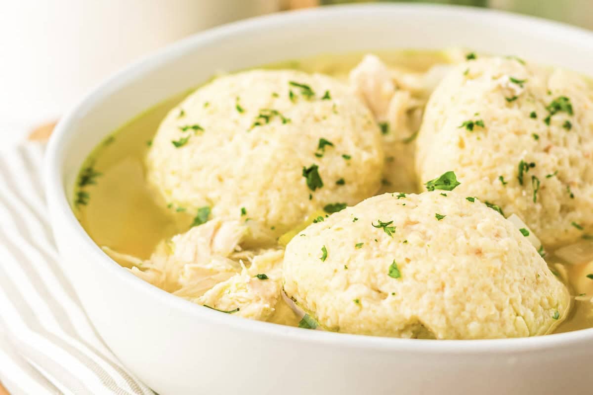 Three large matzo balls in chicken soup, garnished with chopped parsley in a white bowl—an inviting Matzo Ball Soup recipe perfect for your slow cooker.