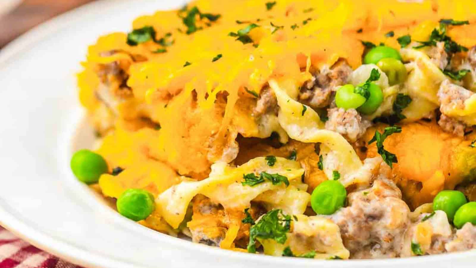 A plate of cheesy casserole with ground meat, egg noodles, green peas, and fresh parsley.