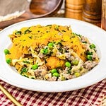 A plate of Amish Country Casserole with cheesy noodles, ground meat, and peas, garnished with chopped parsley.