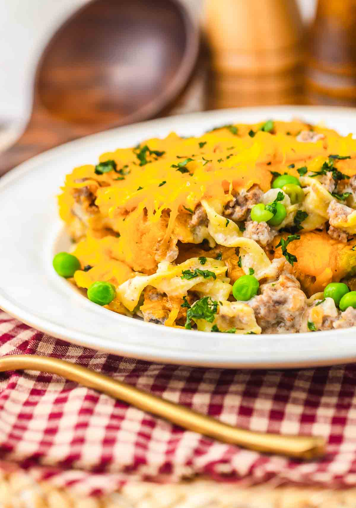 A plate of Amish Country Casserole with ground meat, peas, melted cheese, and herbs on top, served on a red checkered cloth.