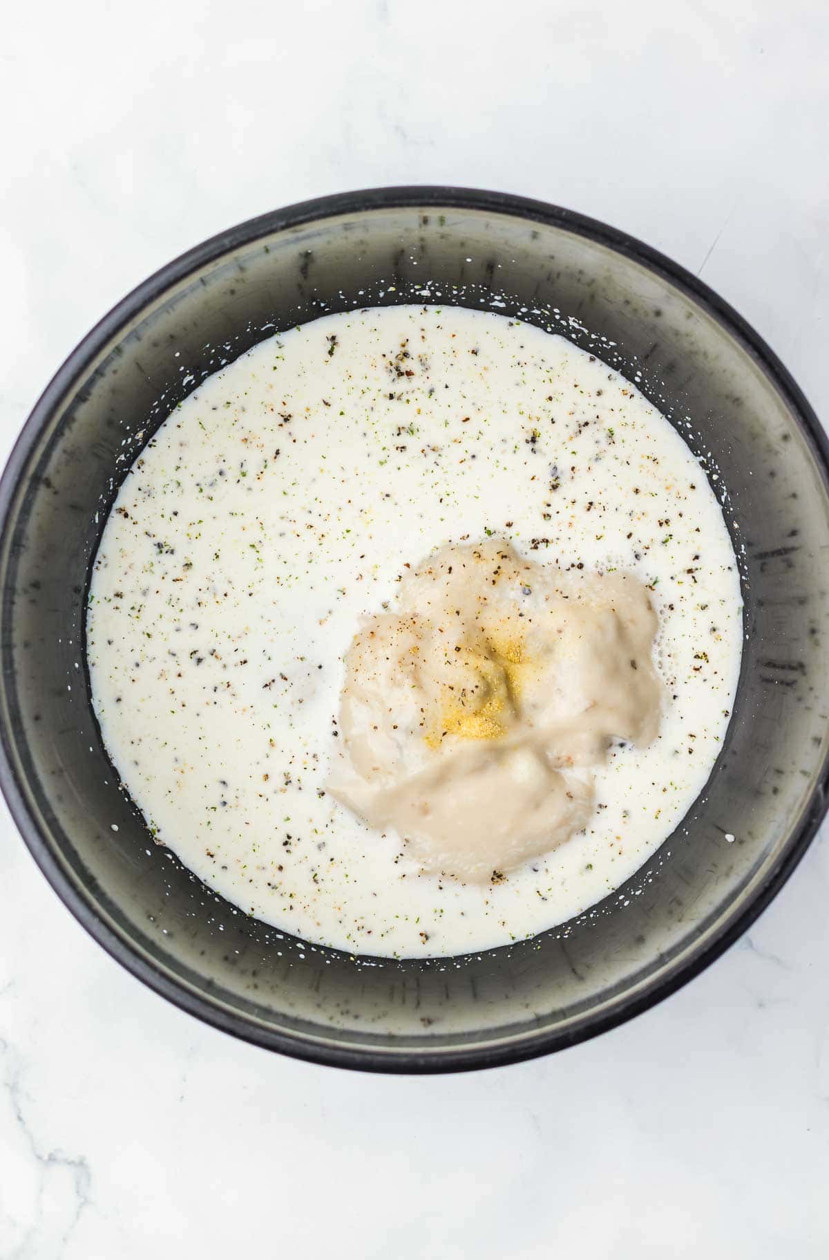 A bowl with milk, black pepper, and a dollop of creamy soup on a white surface&mdash;perfect beginnings for an Amish Country Casserole.