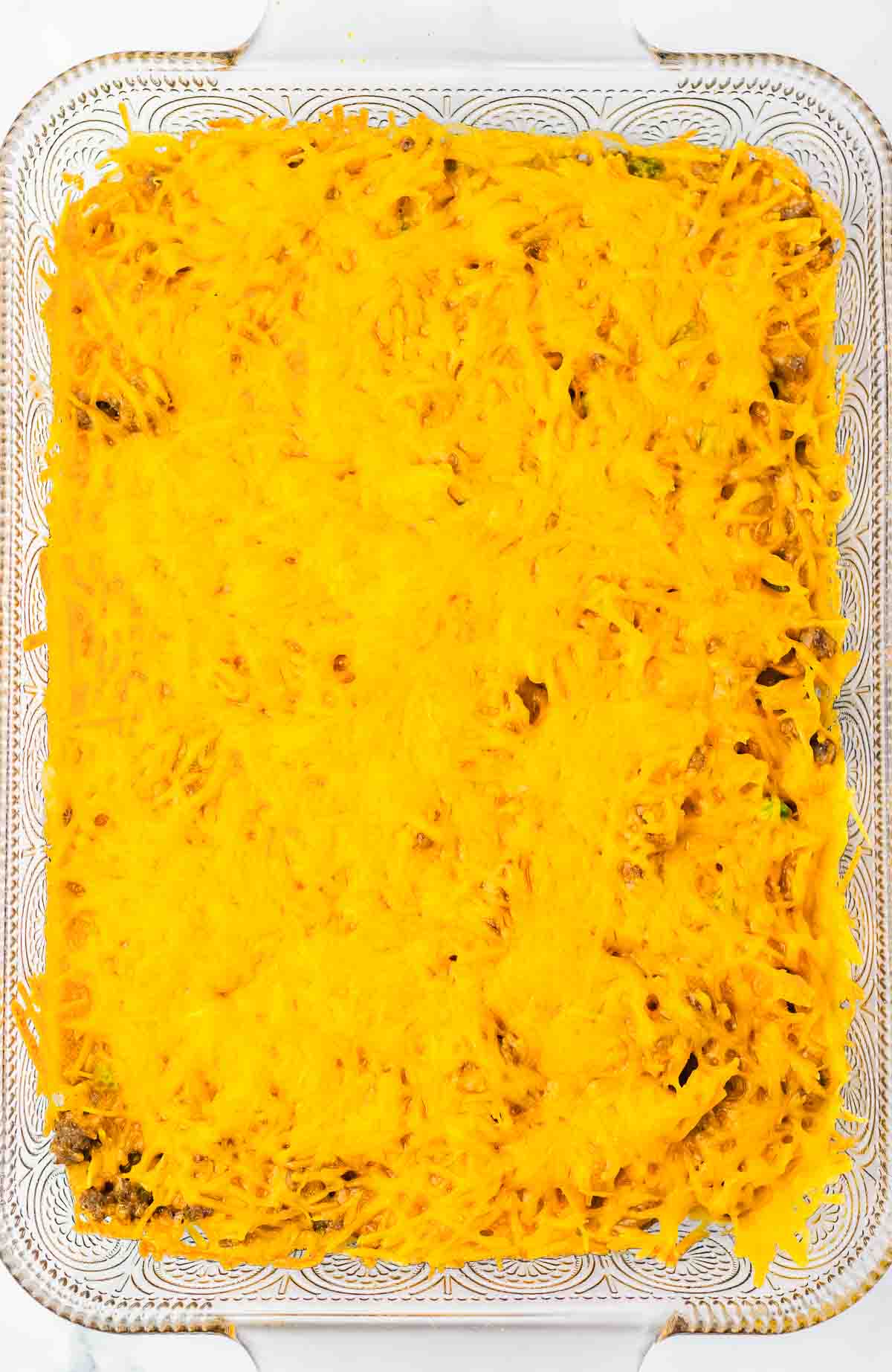 An Amish Country Casserole dish filled with baked food and topped with a golden layer of melted shredded cheddar cheese.