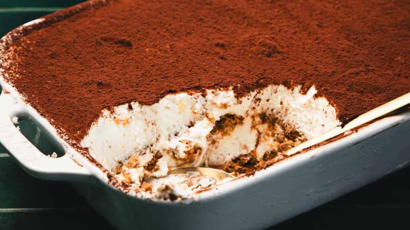 A slice of tiramisu dessert topped with cocoa powder on a plate with a gold-colored fork.