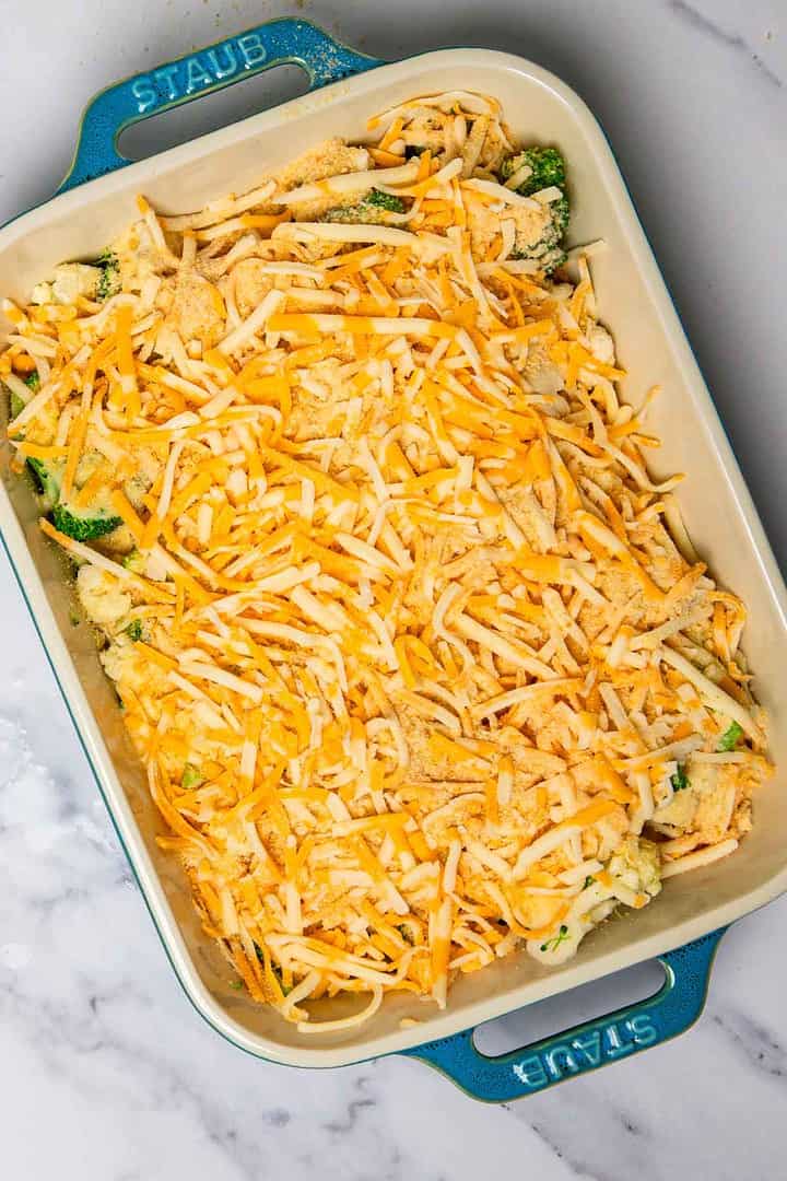 Cheese casserole dish filled with broccoli and shredded cheese sits on a marble countertop.