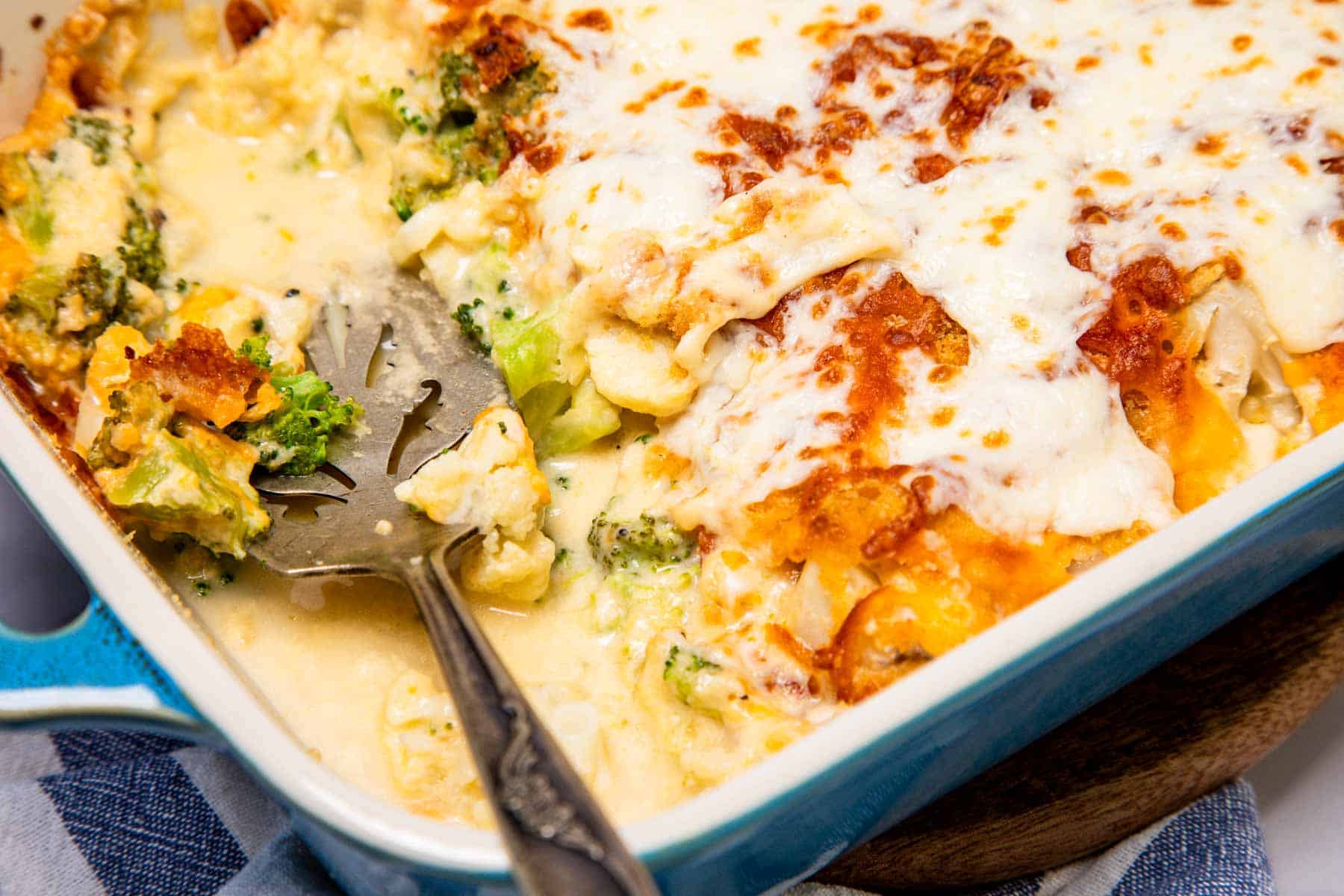 Cheese casserole loaded with broccoli and cauliflower, topped with a golden baked cheese crust in a vibrant blue dish.