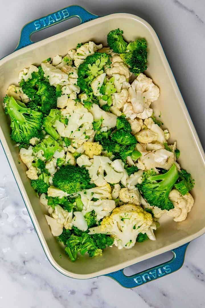Casserole dish filled with steamed broccoli and cauliflower florets, perfect for a healthy cheese casserole, sits on a marble countertop.
