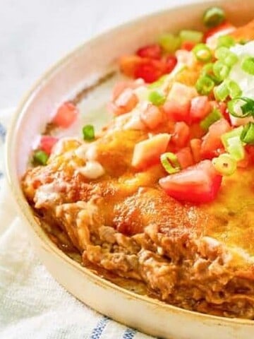 A plate of cheesy enchiladas topped with sour cream, diced tomatoes, and chopped green onions.