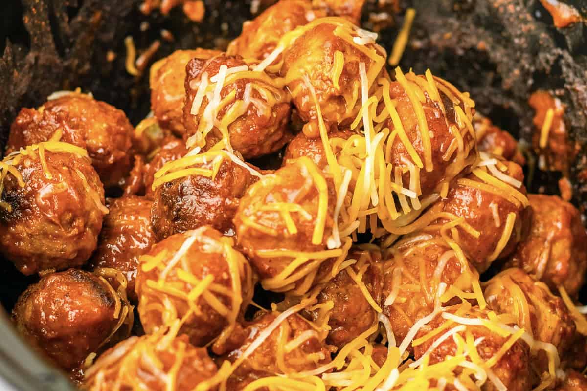 Tender 4 ingredient enchilada meatballs coated in a rich sauce and topped with shredded cheese, served in a dark dish. Perfect for the slow cooker!.