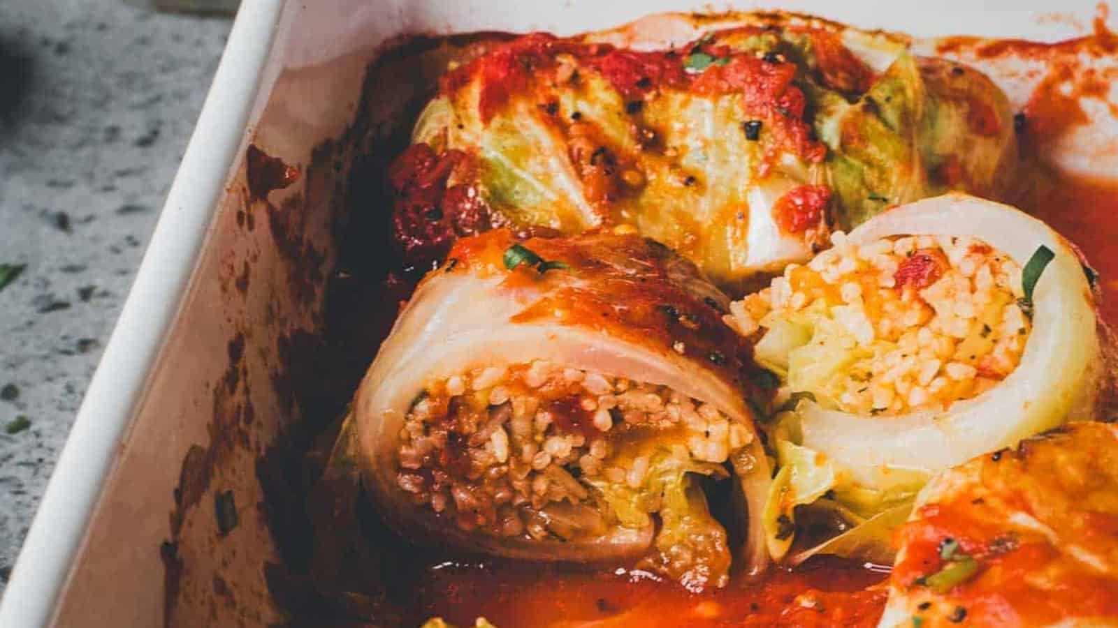 Stuffed cabbage rolls filled with rice and meat in tomato sauce inside a white baking dish.