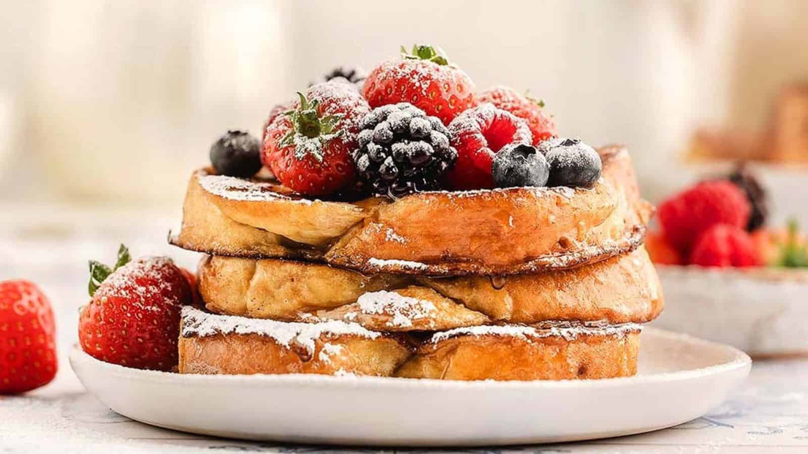 Three slices of French toast topped with powdered sugar, strawberries, blackberries, and blueberries.