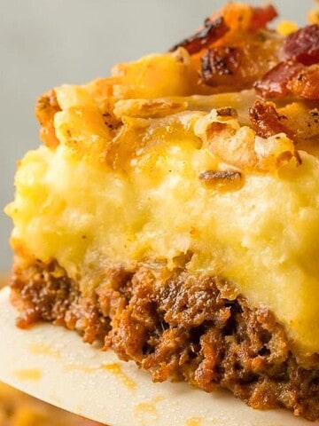 A close-up of a slice of shepherd's pie with ground meat, mashed potatoes, cheese, and bacon on a spatula.