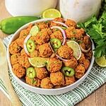 A bowl of spicy meatballs, inspired by birria flavors, garnished with lime slices, jalapeños, red onion, and fresh herbs.