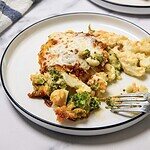 A serving of cheesy broccoli and cauliflower casserole, made from a classic cheese casserole recipe, sits on a white plate with a fork.