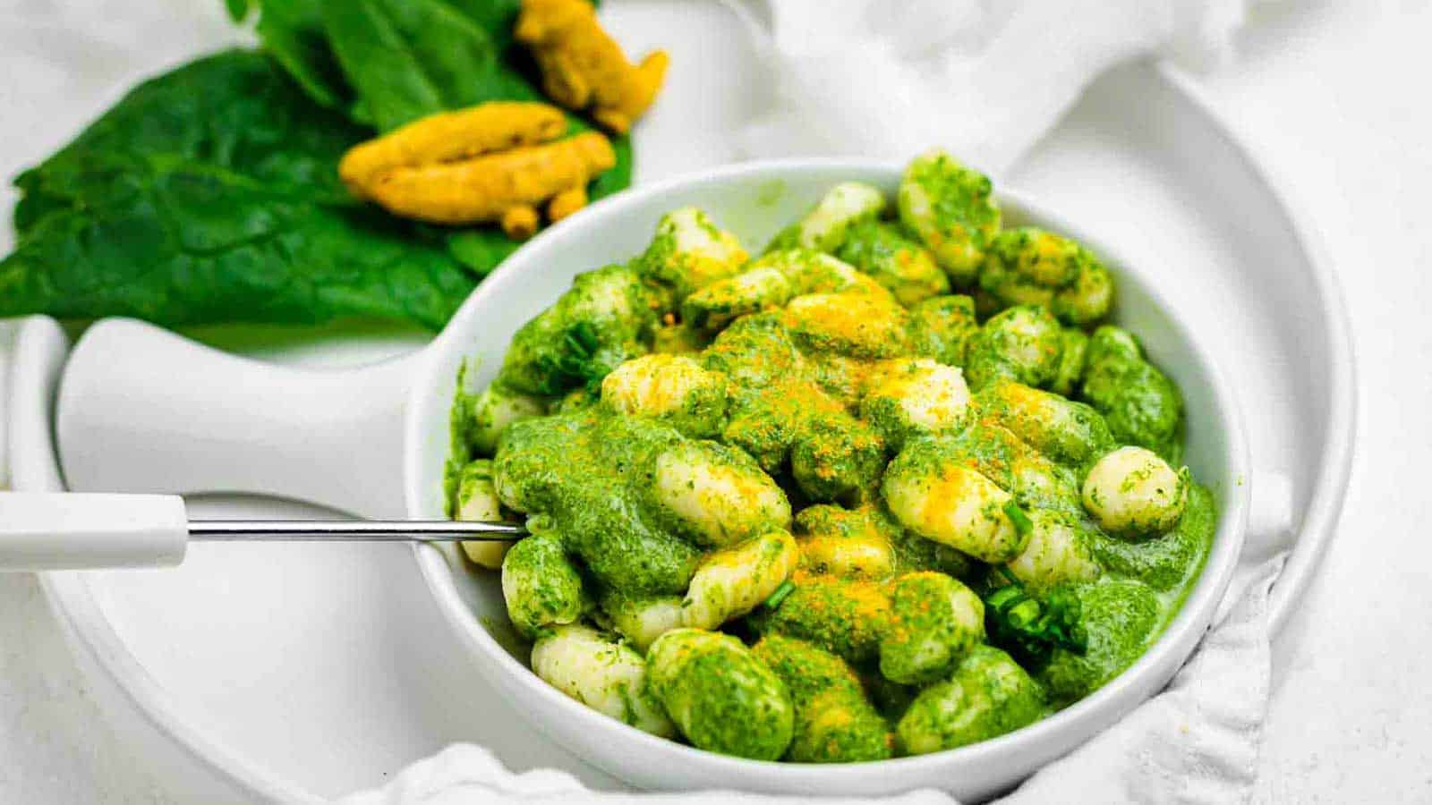 Bowl of gnocchi covered in green pesto sauce, topped with yellow seasoning, on a white plate&mdash;a perfect addition to your collection of tasty recipes or festive green recipes for St. Patrick&rsquo;s Day.