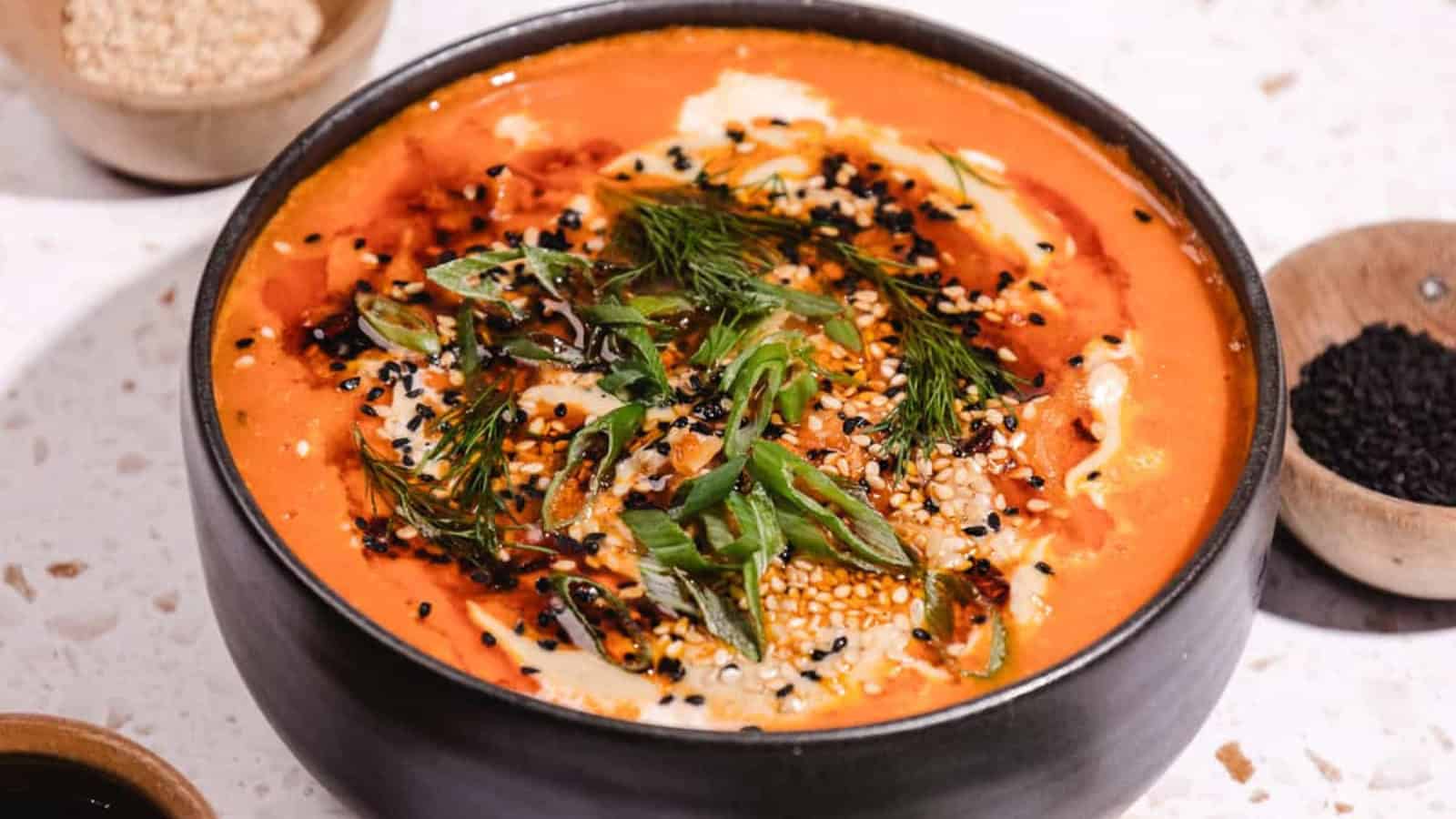 Bowl of creamy soup topped with herbs, seeds, and spices, with fresh dill and green onions on the side.