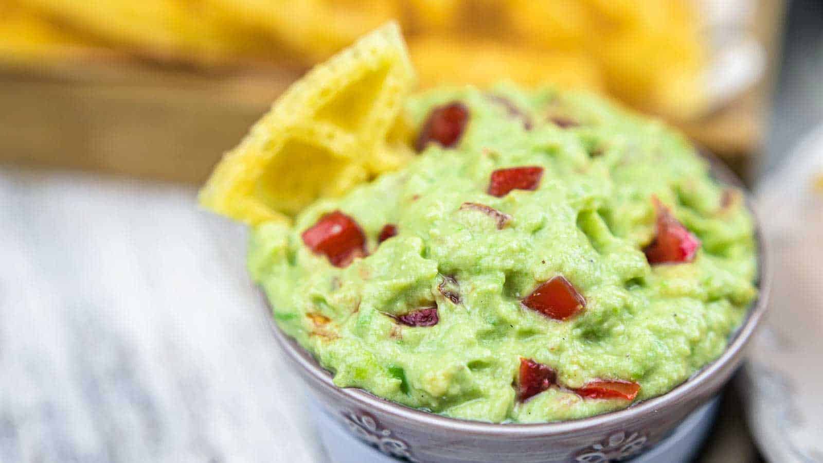 Bowl of guacamole with diced tomatoes, topped with tortilla chips&mdash;a perfect addition to your Green recipes collection for a fresh and festive touch.