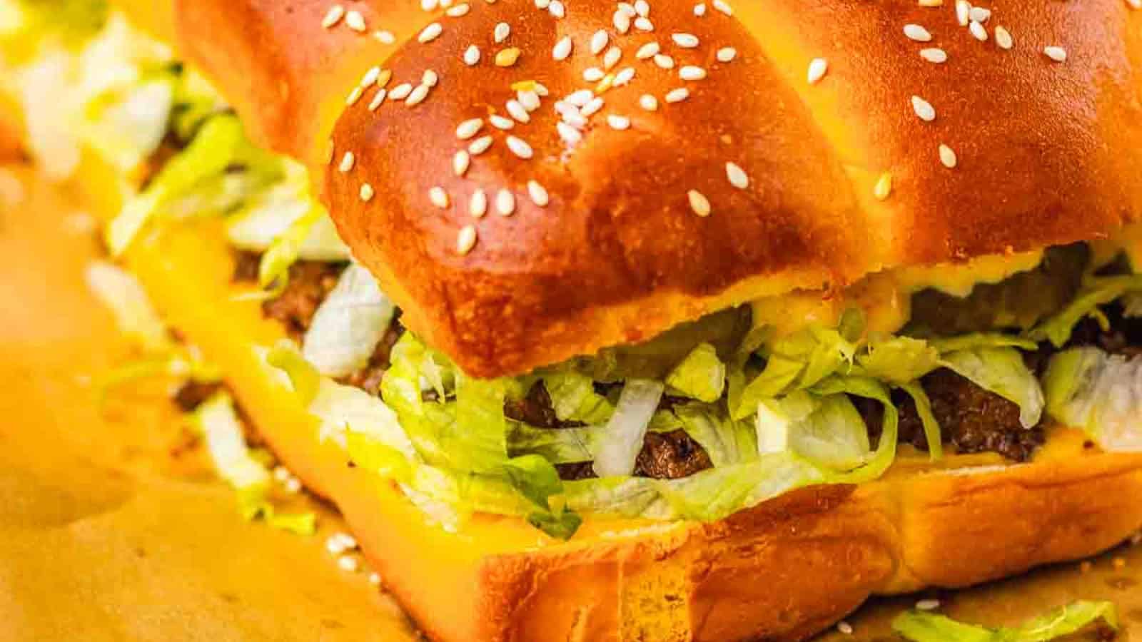 Four cheeseburger sliders with lettuce and pickles on a white plate, topped with sesame seed buns.