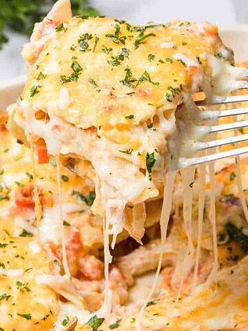 A cheesy baked casserole with herbs being lifted from a dish with a spatula, fresh parsley in the background.