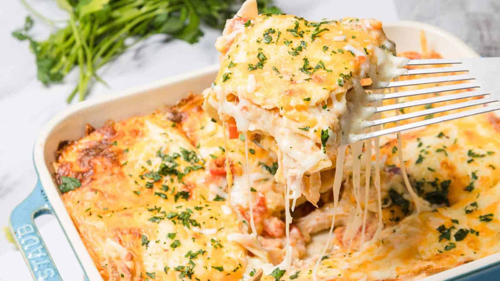 A cheesy baked casserole with herbs being lifted from a dish with a spatula, fresh parsley in the background.