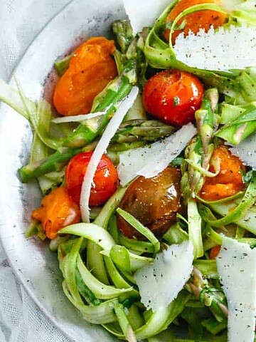 A fresh Spring Salads creation with shaved asparagus, cherry tomatoes, and cheese shavings, served in a silver bowl with a spoon.