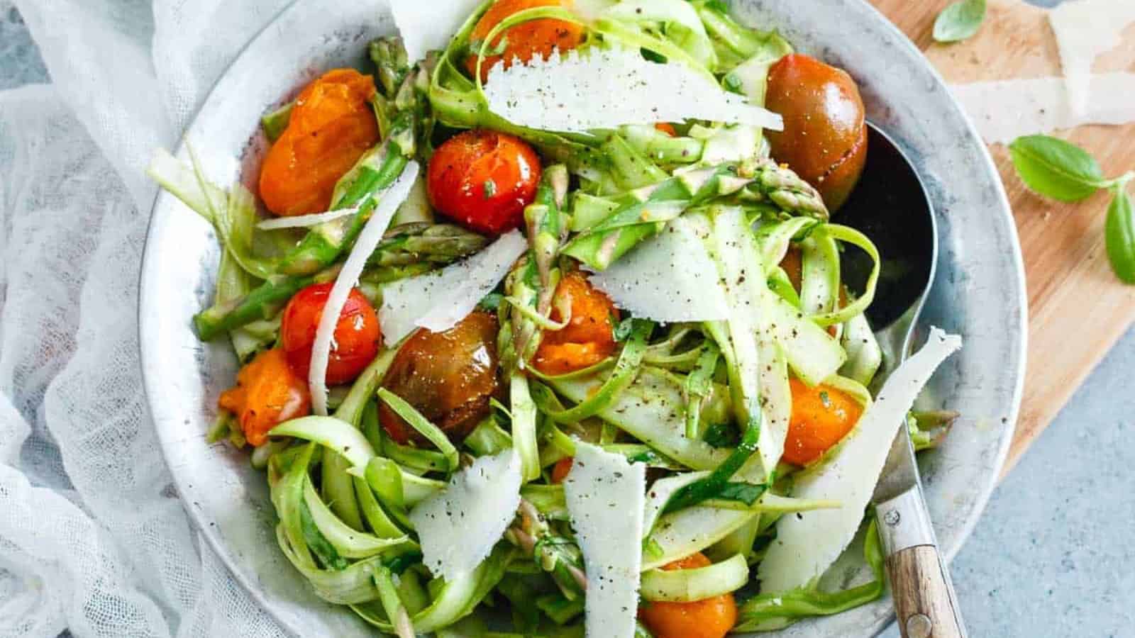 A fresh Spring Salads creation with shaved asparagus, cherry tomatoes, and cheese shavings, served in a silver bowl with a spoon.