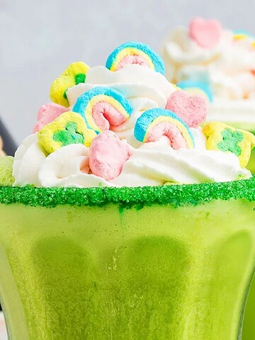Two green milkshakes with whipped cream, colorful marshmallows, and a Baileys bottle in the background.