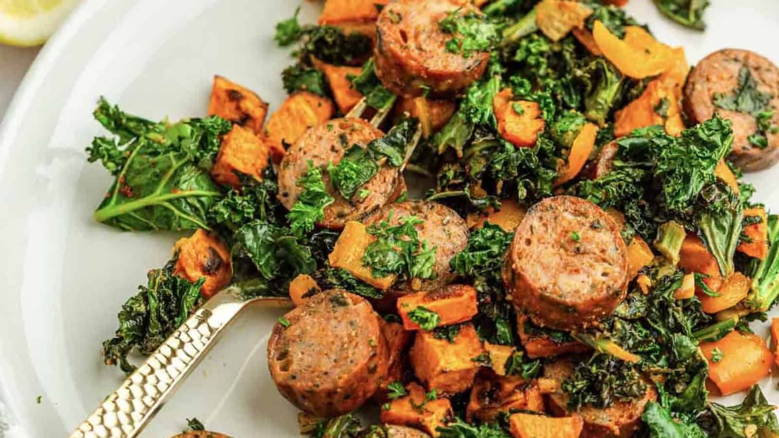 Sliced sausage, kale, and roasted sweet potatoes on a white plate with a gold fork.