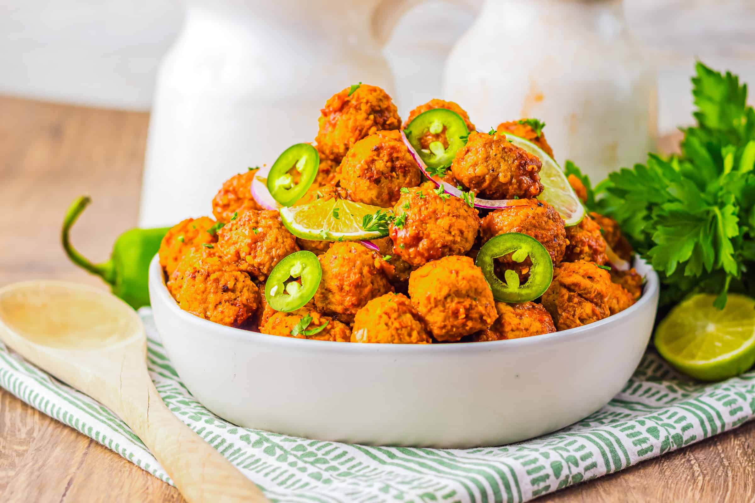 A bowl of spicy falafel garnished with lime slices, red onion, and jalape&ntilde;o peppers sits on a patterned cloth&mdash;perfect alongside slow cooker birria meatballs for a flavorful spread.