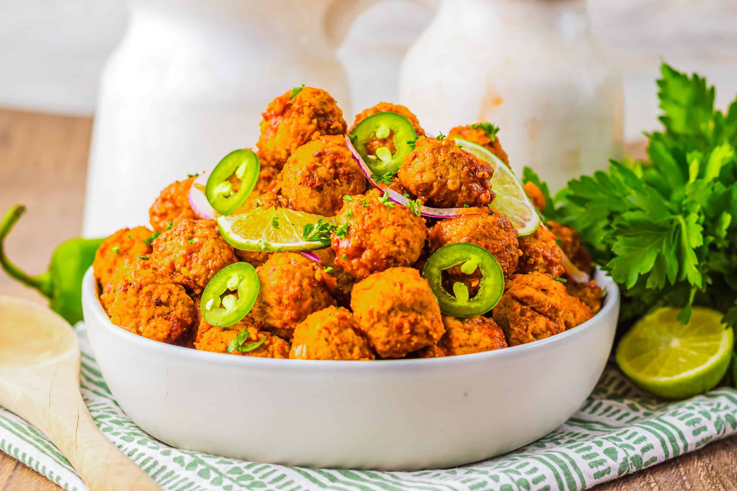 A bowl of spicy falafel, reminiscent of slow cooker meatballs, garnished with lime, jalape&ntilde;o slices, red onion, and fresh parsley.