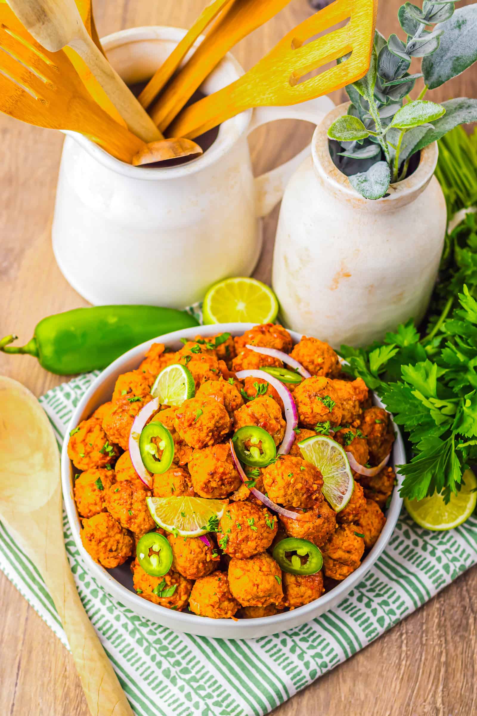 A bowl of spicy falafel garnished with lime, jalape&ntilde;o slices, and red onion sits alongside herbs and utensils&mdash;perfect inspiration for making Birria Meatballs in your slow cooker.