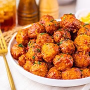 A white bowl filled with saucy enchilada meatballs, made using a simple 4 ingredient slow cooker recipe, sits on a table with a fork beside it.