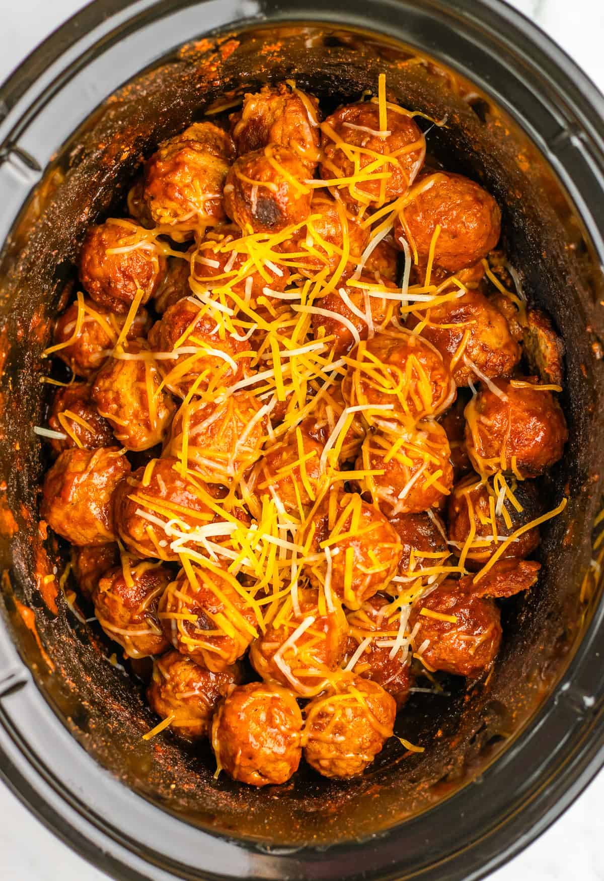 Slow Cooker filled with BBQ meatballs covered in shredded cheddar cheese&mdash;this 4 ingredient enchilada meatball recipe is perfect for easy, flavorful gatherings.