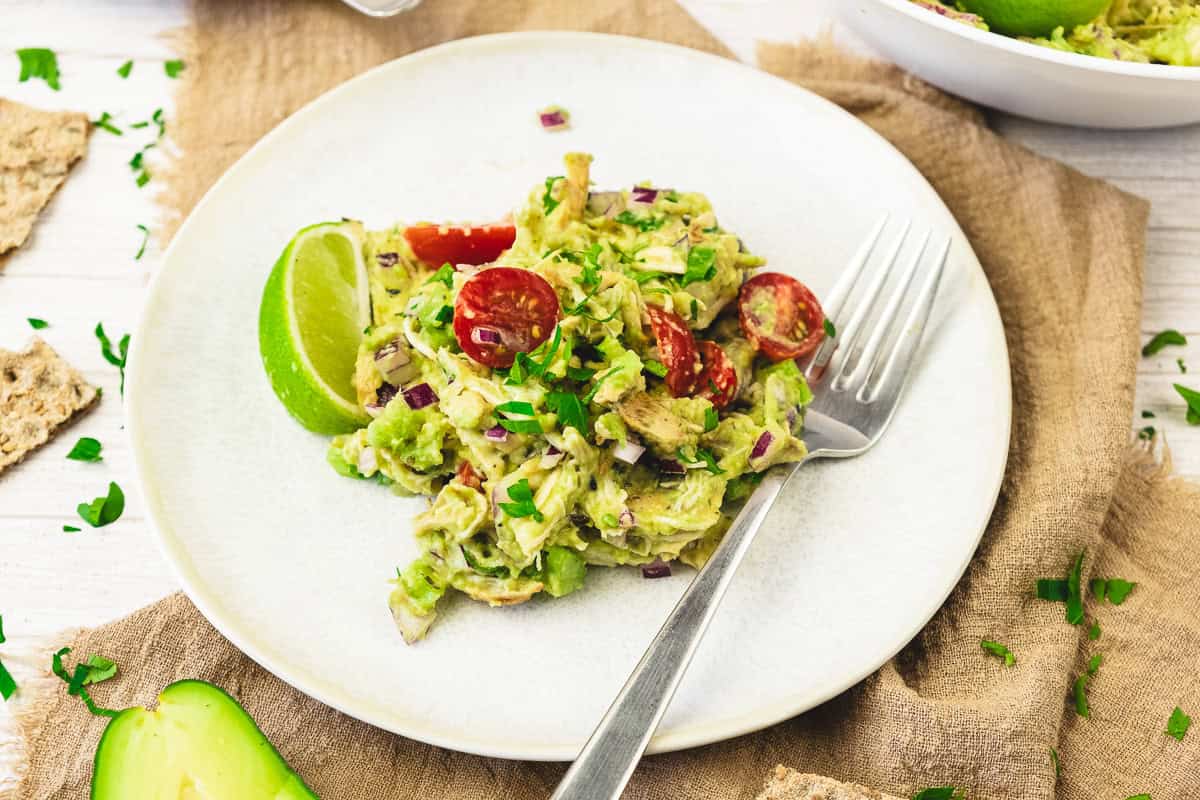 A plate of avocado chicken salad with cherry tomatoes, red onion, a lime wedge, and a fork—this fresh chicken salad recipe is perfect for any meal.