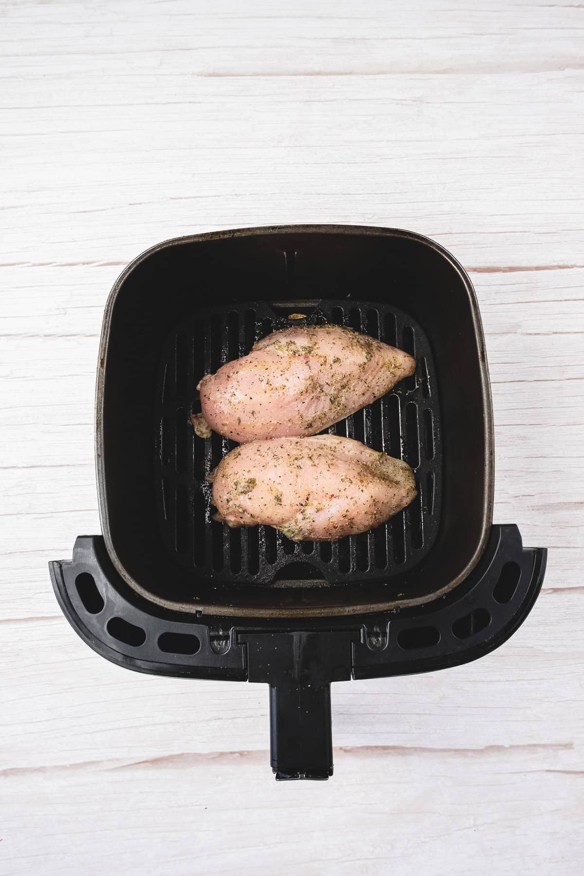 Two seasoned raw chicken breasts placed inside an air fryer basket on a light wooden surface—perfect for your next chicken salad recipe.