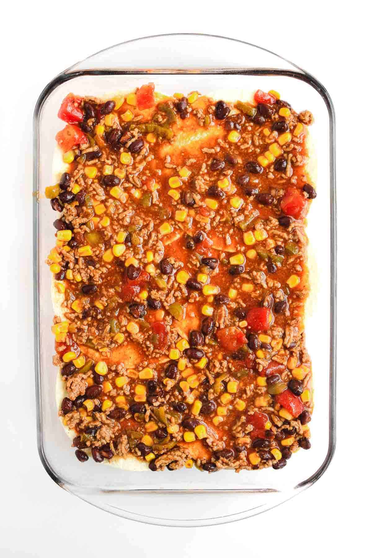 Rectangular glass dish with a layered Beef Enchilada Casserole of ground beef, corn, black beans, and diced tomatoes&mdash;a comforting casserole recipe perfect for any meal.