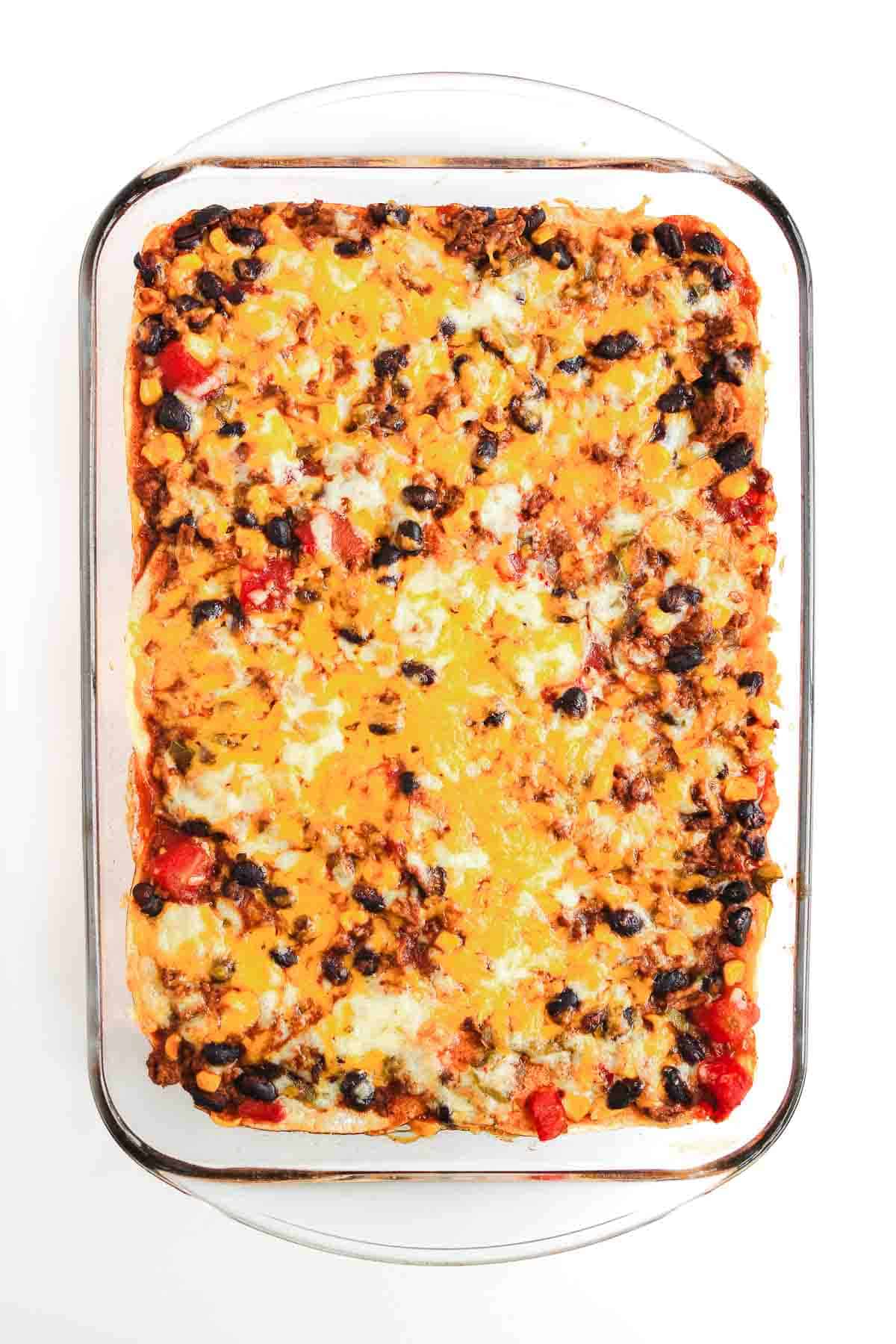 A delicious Beef Enchilada Casserole recipe featuring layers of black beans, diced red peppers, and melted cheese, baked to perfection in a glass dish.