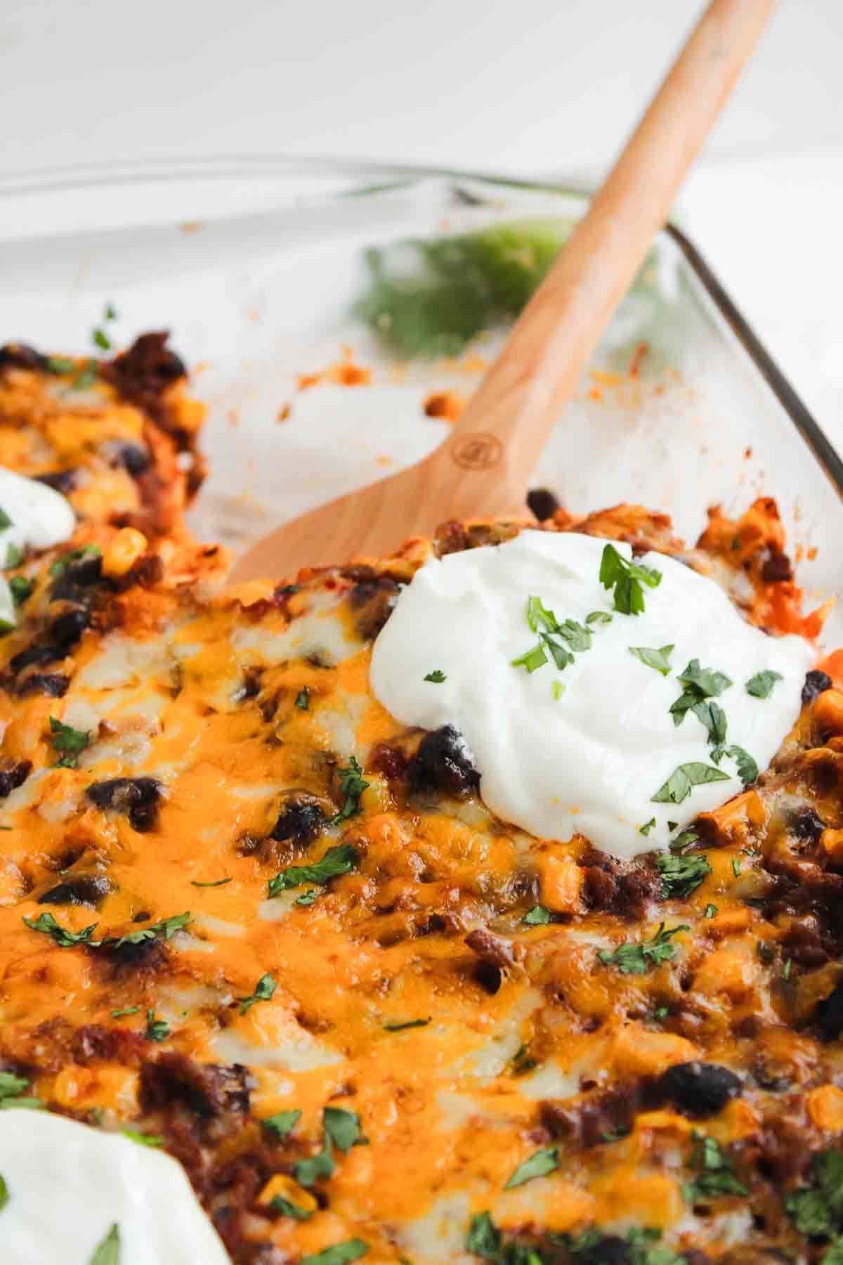 A cheesy beef enchilada casserole with black beans, corn, and melted cheese, topped with sour cream and chopped herbs.