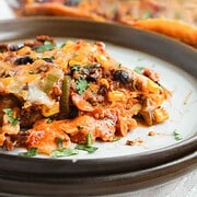Close-up of cheesy Beef Enchilada Casserole with beans and vegetables on a plate, with a baking dish in the background—a must-try casserole recipe for any Mexican food lover.