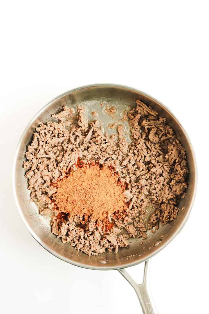 Cooked ground beef in a skillet with a pile of taco seasoning in the center, ready to be mixed&mdash;perfect for starting your favorite Beef Enchilada Casserole.