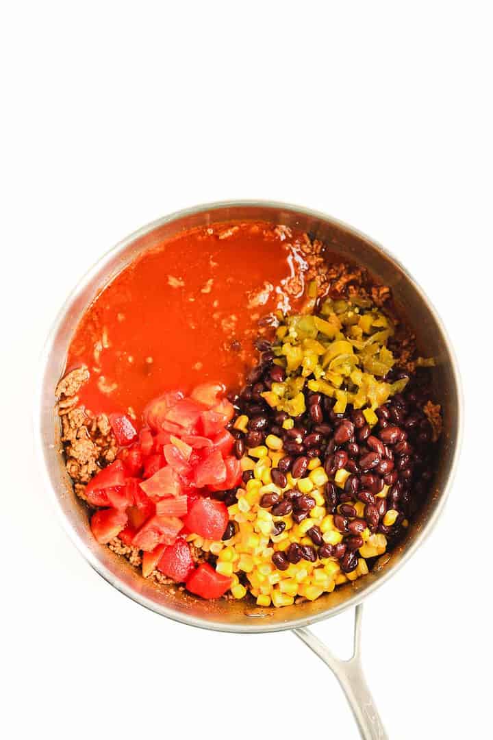 Overhead view of a pot with ground beef, tomato sauce, diced tomatoes, black beans, corn, and green chilies&mdash;perfect for making a hearty Beef Enchilada Casserole.